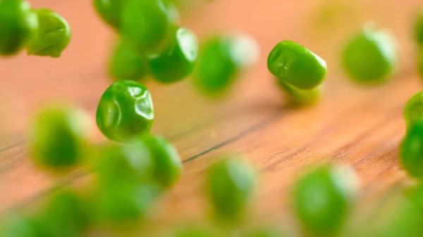 MACRO, DOF: Raw homegrown green peas bouncing off the wooden kitchen table. —  Fotos de Stock