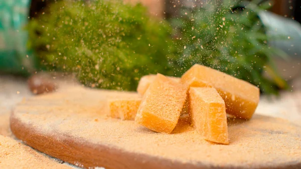 MACRO: Parmesan flakes fall on the cheese cubes on the wooden board. — Photo