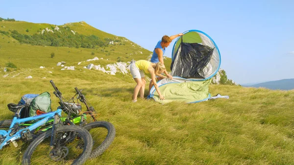 Cheerful active couple setting up a tent in the big empty meadow on a mountain — Stock Photo, Image