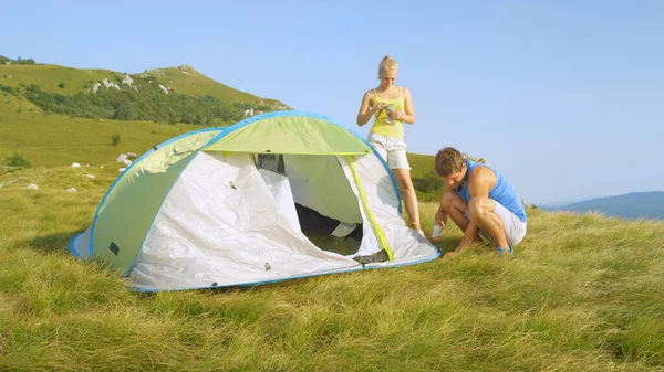 Donna bionda sportiva che aiuta il suo fidanzato atletico mentre installa la loro tenda. — Foto Stock