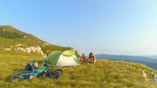 DRONE: Allegro turista in mountain bike nelle Alpi prepara una tenda nel prato. — Foto Stock