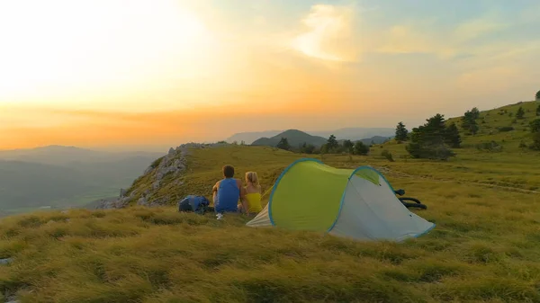 AERIALE: Giovani coppie attive sedute vicino alla tenda e che guardano il tramonto. — Foto Stock