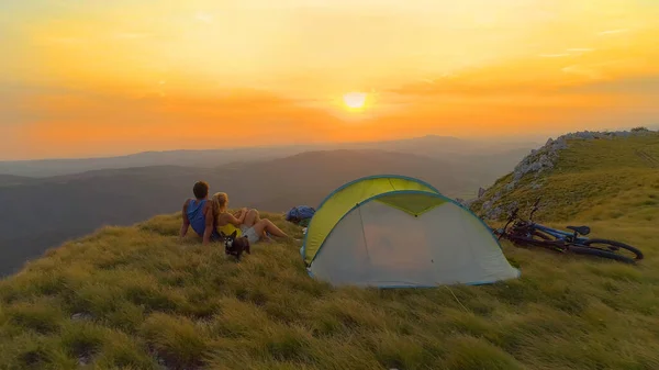 AEREO: Raggi di sole dorati brillano su cucciolo e coppia coccolati dalla tenda al tramonto. — Foto Stock