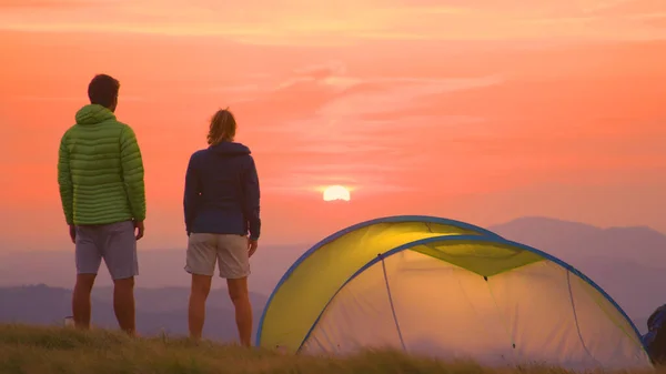 COPY SPACE: Man and woman in windbreakers stand by tent and watch the sunrise. — Foto de Stock