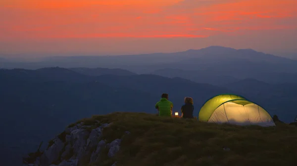 Tourist couple camping in the Alps sit by the lantern and talk on a calm evening — Stock Photo, Image