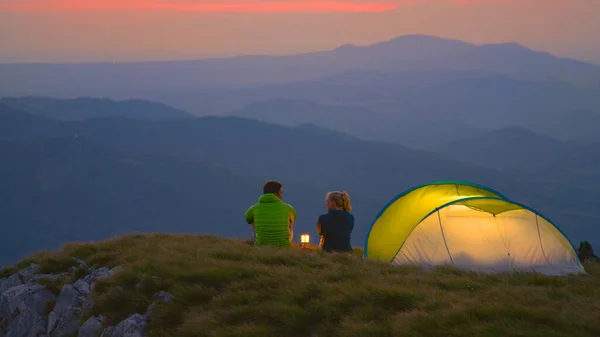 Young hiker couple sitting and talking by the lantern on a cold summer morning — Foto de Stock