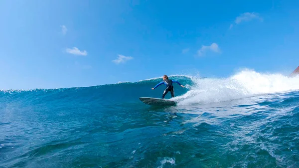 LOW ANGLE: Athletic surfer dude splashes water while carving a blue tubing wave — Photo