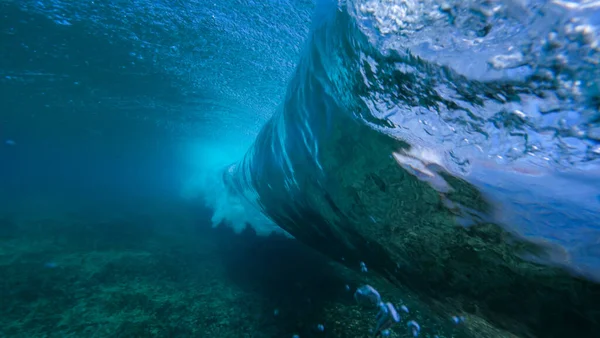 UNDERWATER: Large deep blue ocean waves breaking and splashing over the camera. — стоковое фото