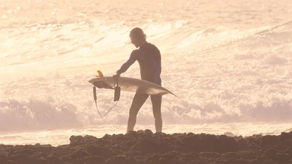 SILHOUETTE: Droppande våt surfare i våtdräkt går på stenig strand med surfbräda — Stockfoto