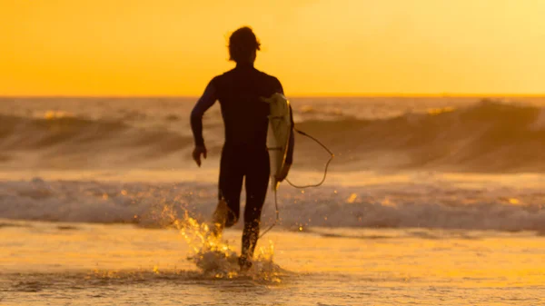 SILHOUETTE:海に向かって走っている間にサーフボードを持っているサーファー男. — ストック写真