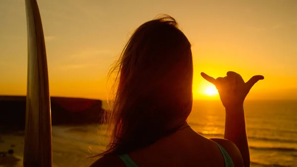 CLOSE UP: Cool surfer girl gives the shaka sign while watching the sunset. — стоковое фото