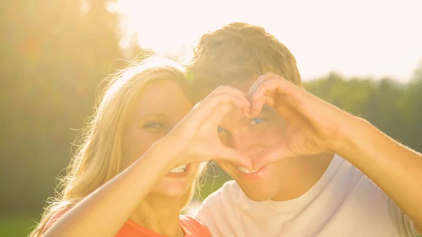 PORTRAIT: Gorgeous girl and her boyfriend making a heart shape with their hands. — Foto de Stock