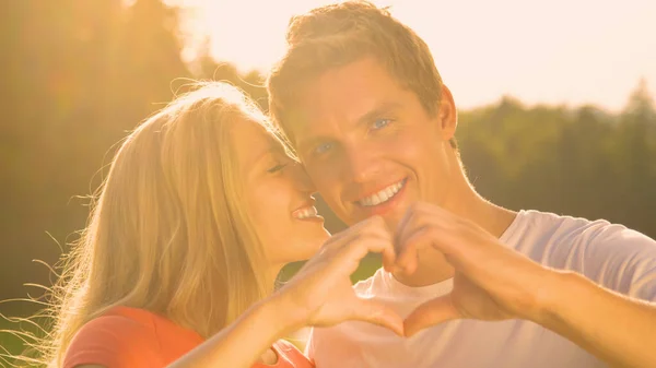 PORTRAIT: Happy man looks at camera while making a heart symbol with girlfriend — Foto de Stock
