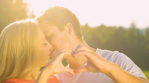 CLOSE UP: Cute couple on date in nature kisses gently while making a heart shape — Foto de Stock