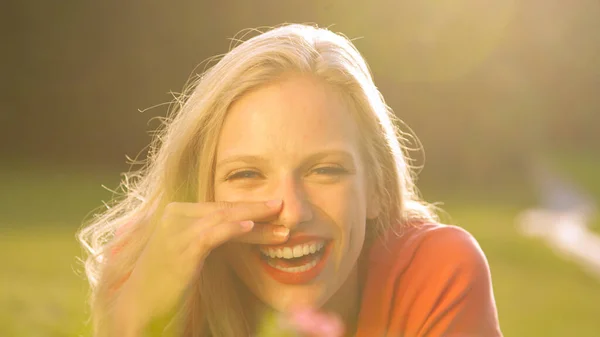 LENS FLARE: Beautiful young woman lying in a meadow and laughing to a joke. — стоковое фото