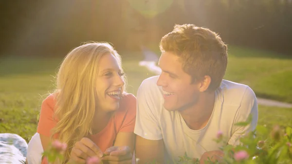 LENS FLARE: Par liggende i græsmarken griner mens du optager en video blog. - Stock-foto