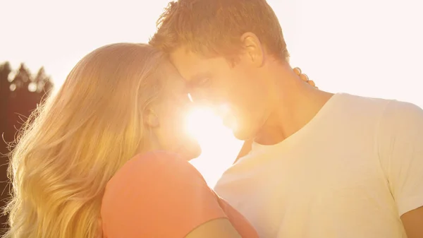 LENS FLARE: Unge elskere rører panden, før de kysser over solnedgangen. - Stock-foto