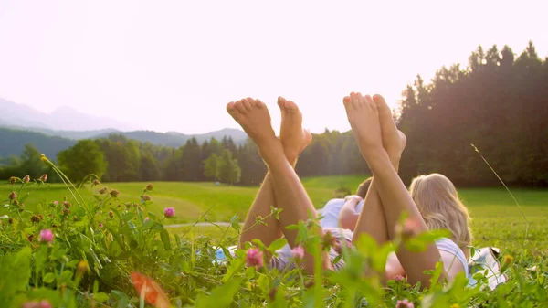 LENS FLARE: Man and woman lying in meadow and playfully kicking their bare feet — стоковое фото