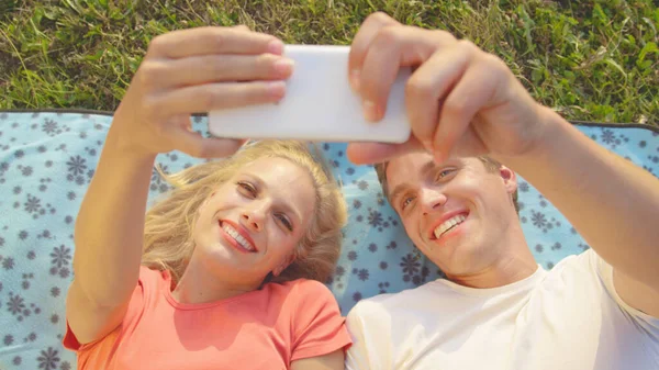CLOSE UP: Cheerful couple laughing and taking selfies while lying on a blanket. — Foto de Stock