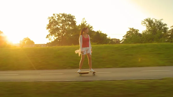 LENS FLARE: Vrolijke vrouw op een skateboard door het park op een zonnige dag. — Stockfoto