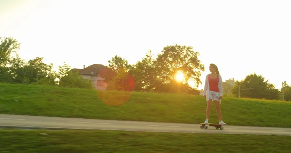 SUN FLARE: Безтурботний жіночий скейтбордист їде на дошці в сонячний ранок . — стокове фото