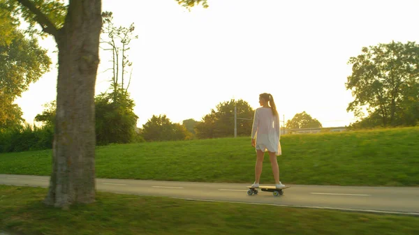 Golden evening sunbeams shine on the happy Caucasian woman riding her skateboard — Foto de Stock