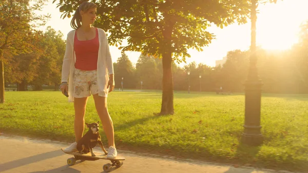 LENS FLARE: Vrolijk meisje en schattige puppy rijden een high tech elektrische longboard. — Stockfoto