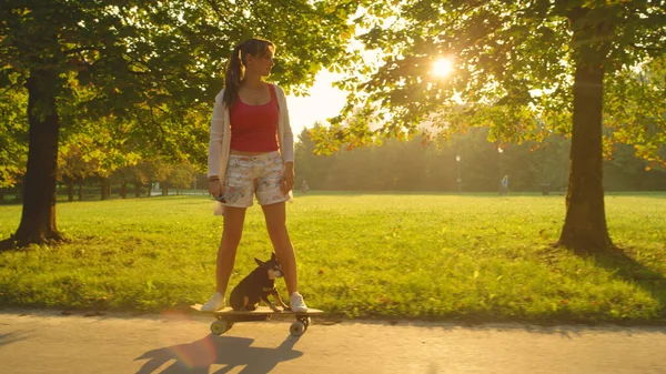 ZON FLARE: Skater meisje paardrijden een elektrische skateboard met haar hond op zonnige dag. — Stockfoto