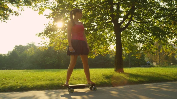 ZON FLARE: Gouden zon schijnt op jonge vrouw rijden een elektrische longboard. — Stockfoto