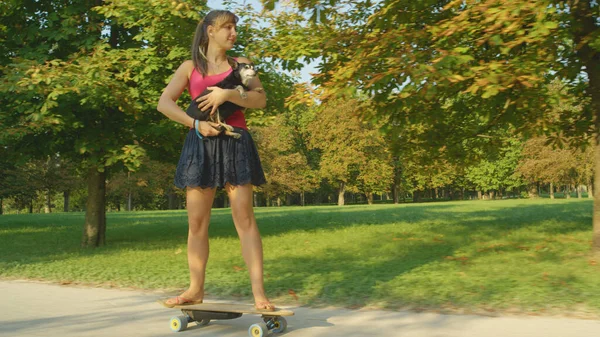 Happy Caucasian woman holding her senior dog while riding her e-skateboard. — Foto de Stock