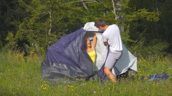 Веселая блондинка развлекается, раздражая своего парня, устанавливая палатку. . — стоковое фото