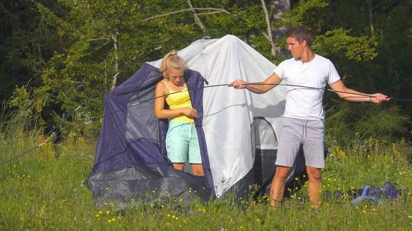 Touristenpaar auf Zeltreise beim Zeltaufbau auf der friedlichen, sonnigen Wiese. — Stockfoto