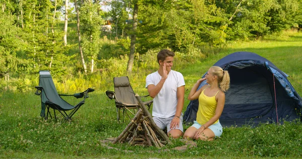 Smiling young woman and man high five after completing a campfire by their tent. — Stock Photo, Image