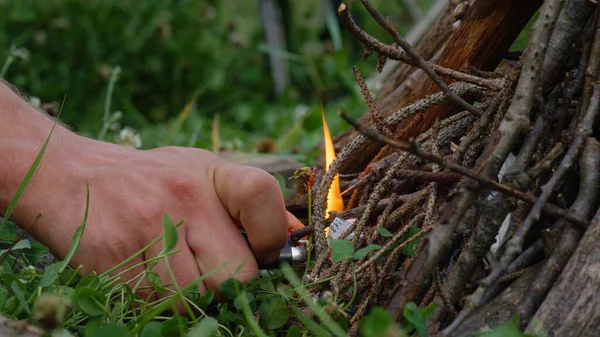 MACRO, DOF: Die Hand des Menschen hält ein Feuerzeug und entzündet ein Lagerfeuer in der Wildnis. — Stockfoto