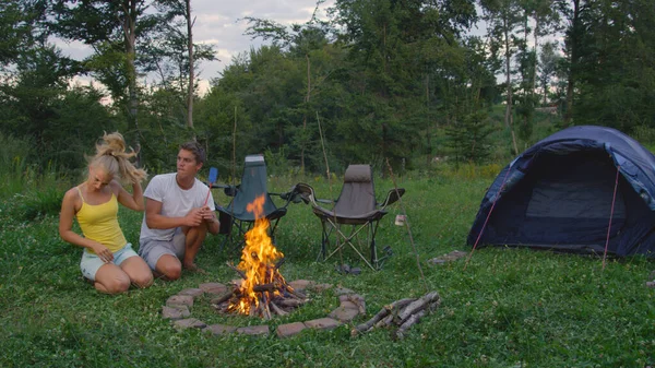 COPY SPACE: Young man and woman sitting by campfire get irritated by pesky bugs. — Stock Photo, Image