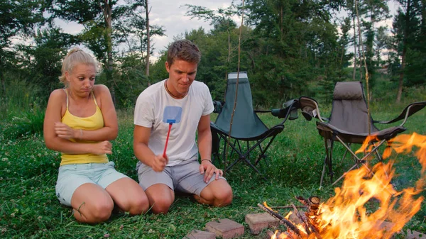 CLOSE UP: Woman gets scared of insect flying close to her while kneeling by fire