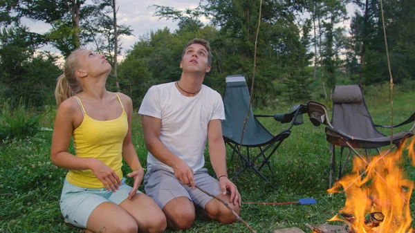 CLOSE UP: Young couple looks up into the dark sky while kneeling by the campfire — Stok fotoğraf