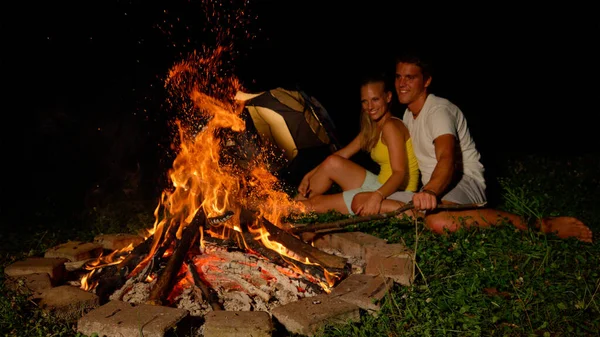 CLOSE UP: Schöner Mann schlägt mit Ast auf das Feuer, während er mit Frau kuschelt. — Stockfoto