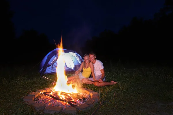 Fogo flamejante sai do fogo como o casal de turistas assar salsichas. — Fotografia de Stock