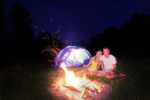 Couple enjoying a camping trip and roasting sausages over the big campfire. — стоковое фото