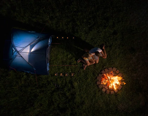 AERIAL: Flug über ein junges Paar, das während eines Campingausflugs am Feuer sitzt. — Stockfoto