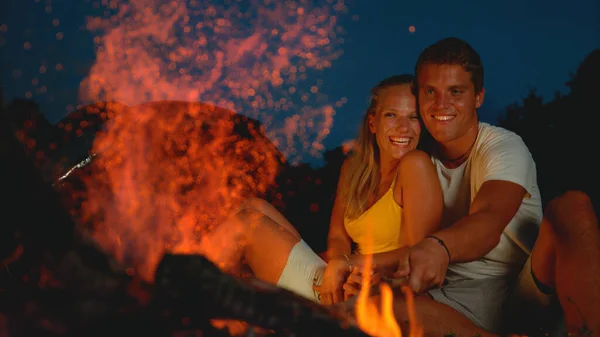 FECHAR UP, DOF: Casal alegre desfrutando de uma noite romântica sentado à beira da fogueira. — Fotografia de Stock