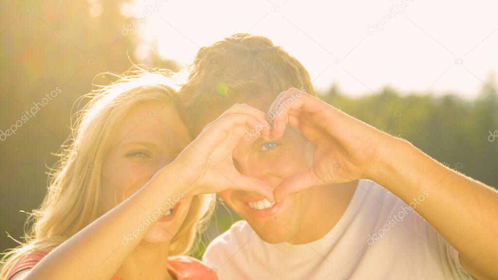 LENS FLARE: Smiling man and woman look through the heart shape they are forming