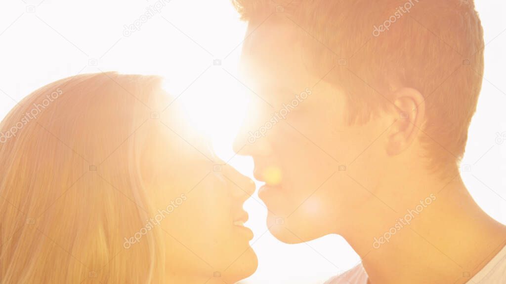 LENS FLARE: Golden sunbeams shine on caring man kissing his girlfriend on nose.