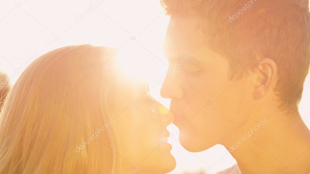 LENS FLARE: Handsome man gently kisses his cheerful girlfriend on the nose.