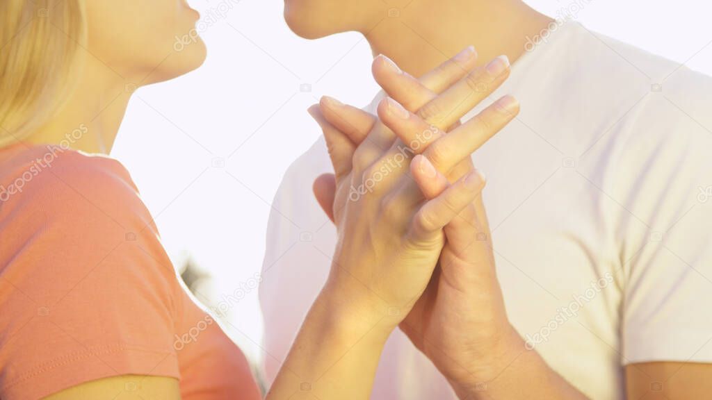 CLOSE UP, DOF: Unrecognizable woman and man interlock fingers while kissing.