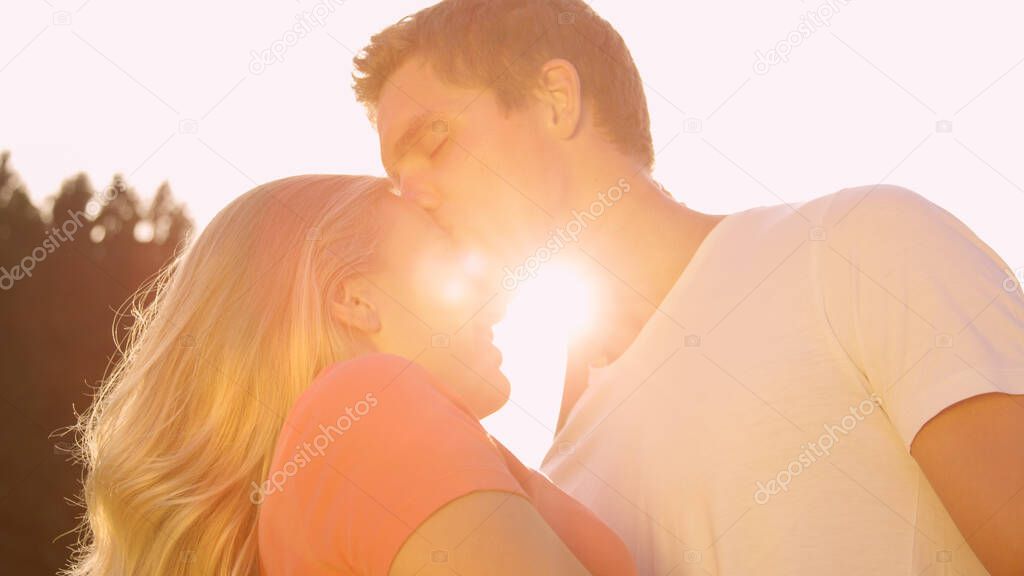 LENS FLARE: Happy man kisses his girlfriend on the forehead on a summer day.