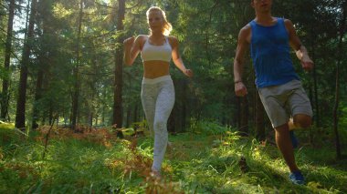 Neşeli sarışın kadın ve erkek arkadaş ladin ormanlarında koşuyor..