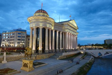 DRONE: Flying above a river flowing past a beautiful ancient building in Skopje.