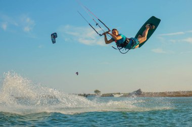 LOW ANGLE: Happy young woman jumps high in the air while kiteboarding in Greece.